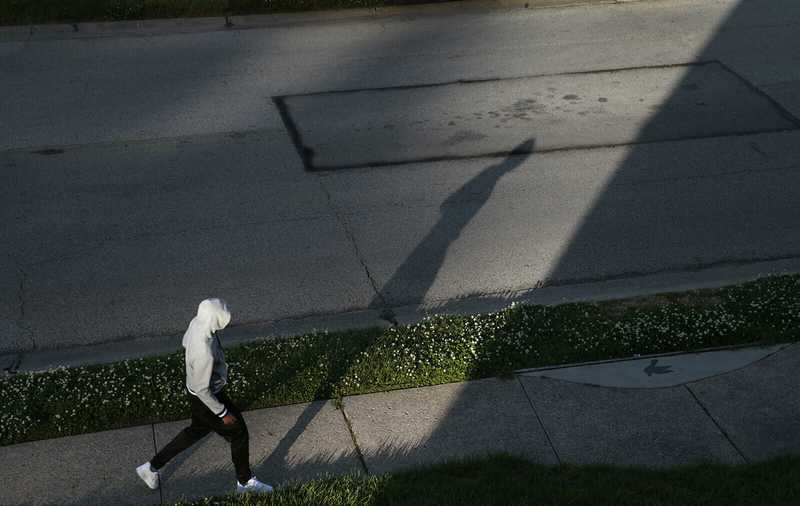A person in a white hoodie walks past the spot where Michael Brown was shot casting a shadow on the pavement.
